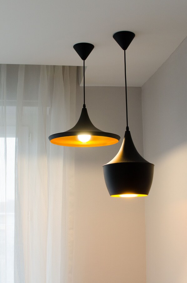 Two pendant lights hanging from the ceiling in a room with a sheer curtain and a light-colored wall.