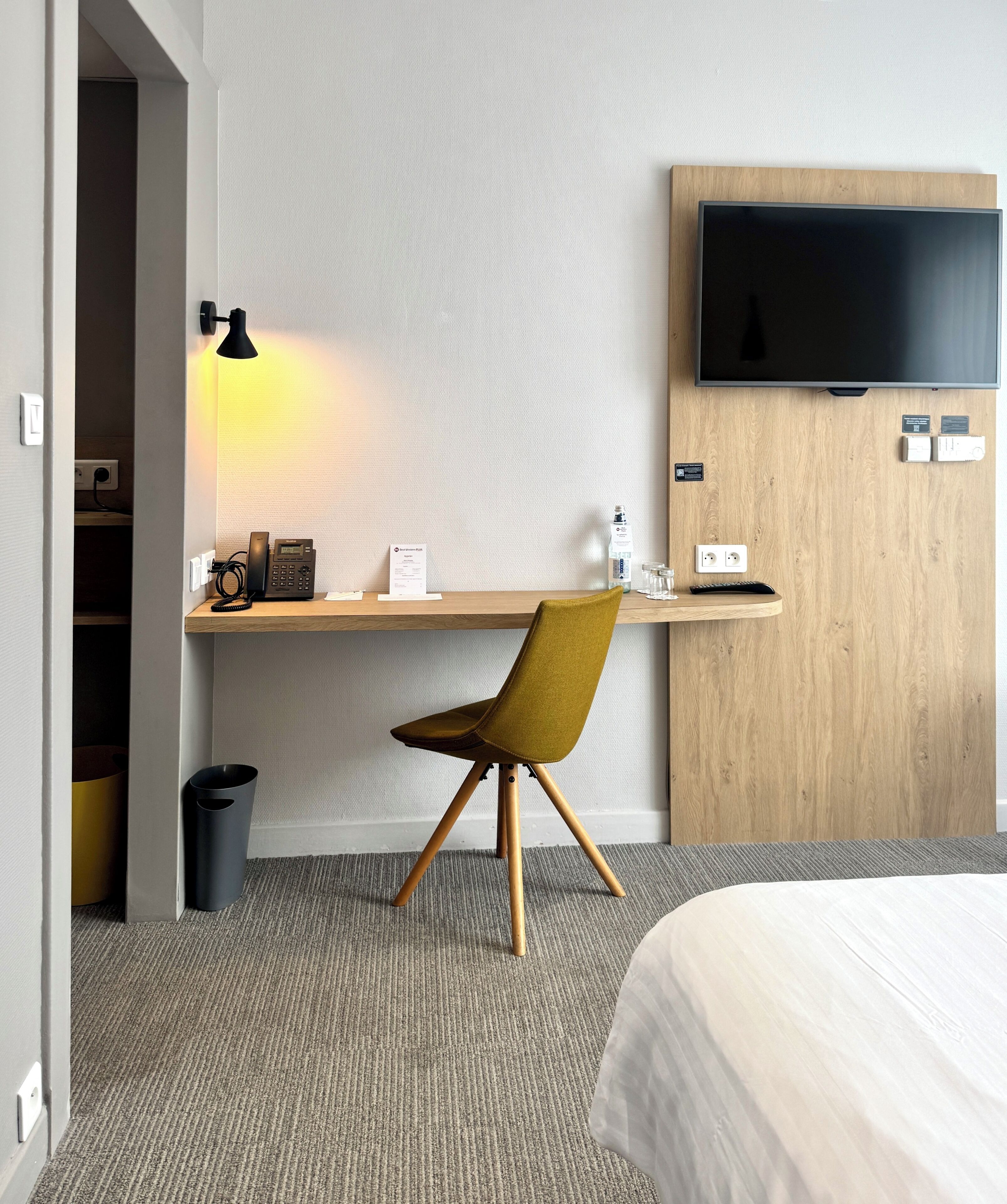Hotellihuone, jossa on sänky, työpöytä tuolilla, televisio ja roskakori.