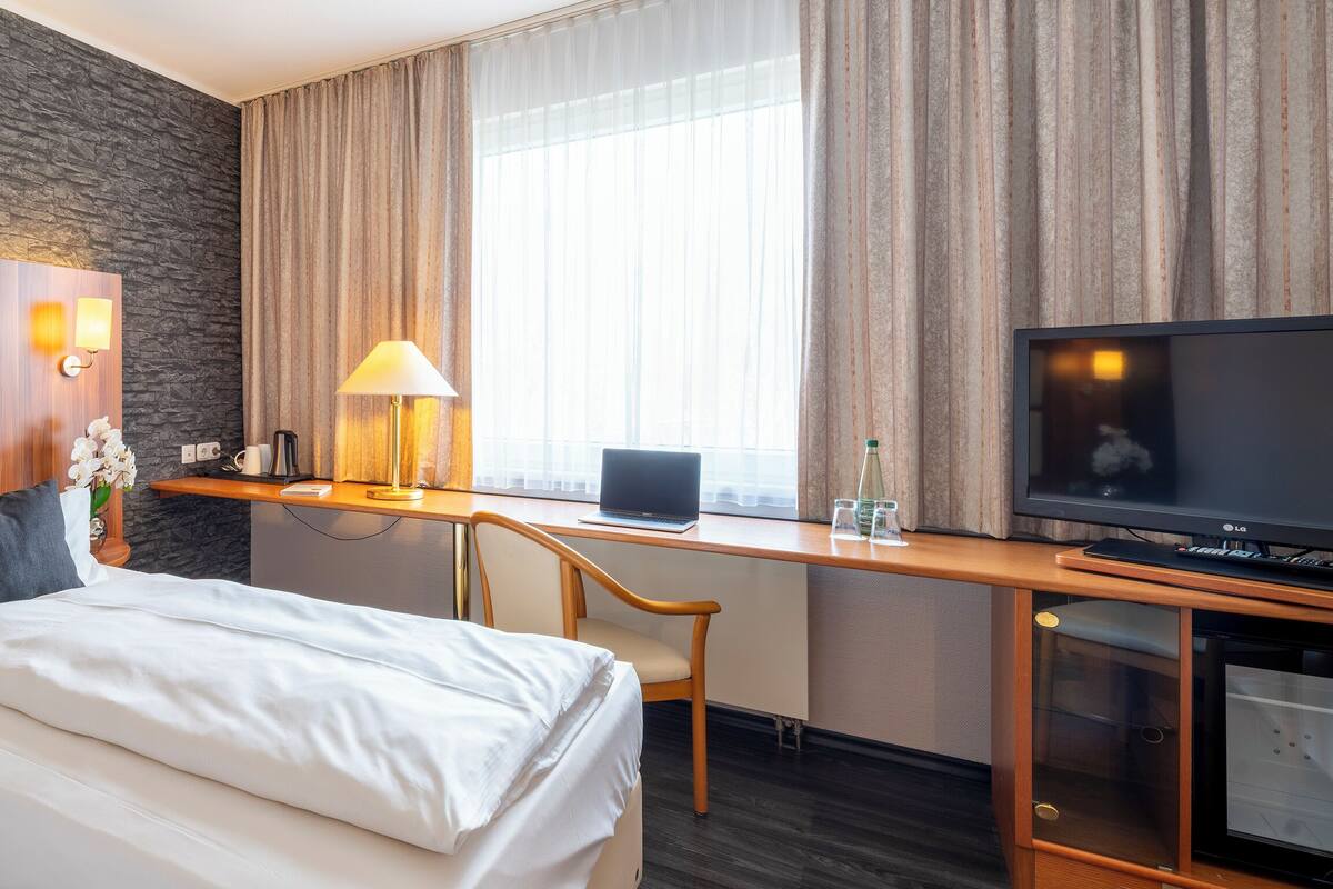 Una habitación de hotel con una cama, un escritorio con una computadora portátil, un televisor y una lámpara.