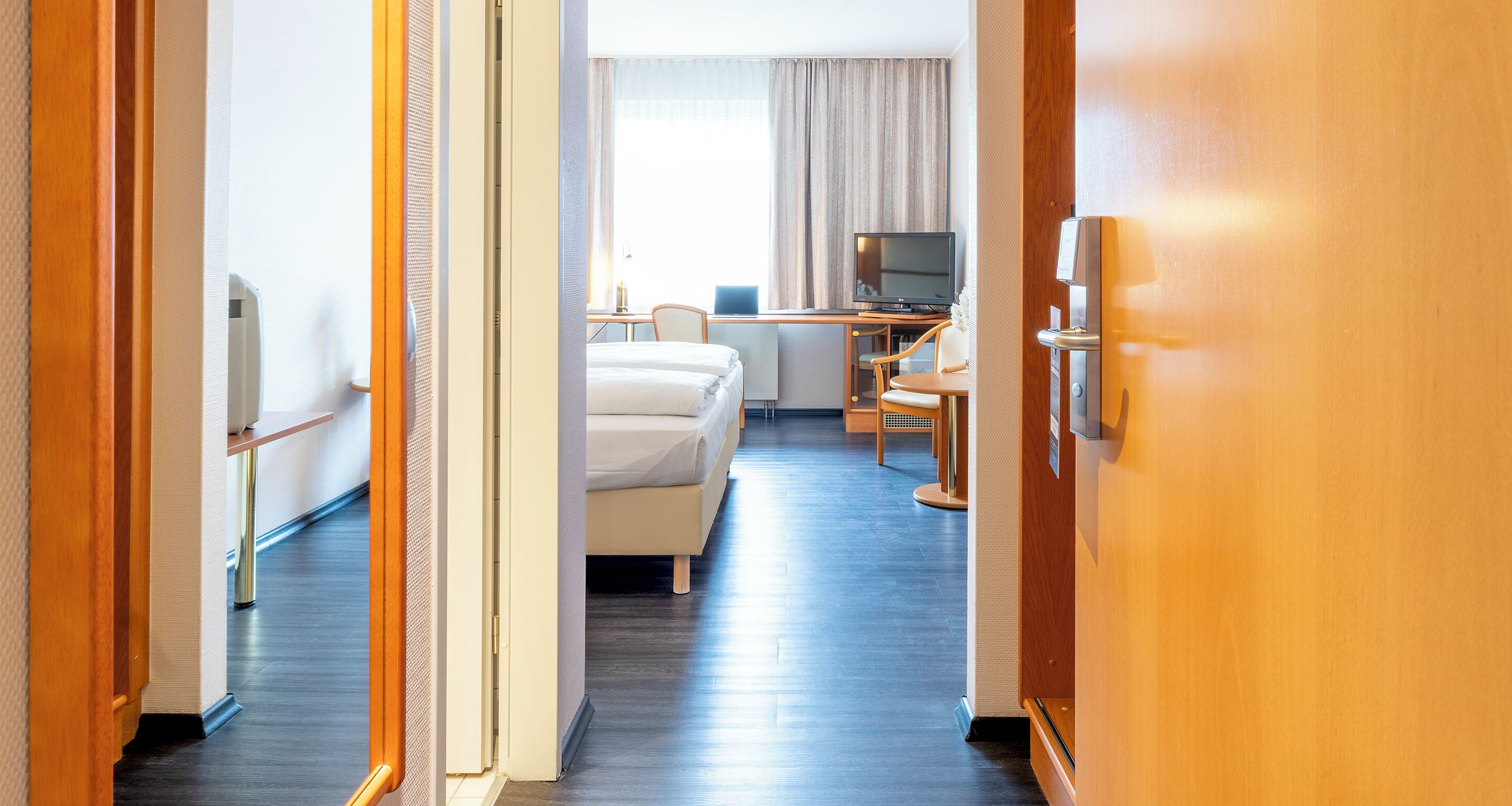 A hotel room with a bed, desk, chair, TV, and a minibar.