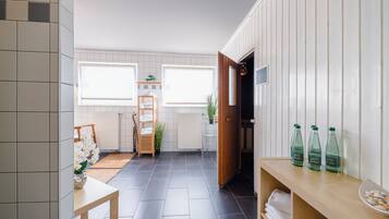A modern bathroom with a tiled floor, a wooden bench, a shelf with bottles, and a towel rack.
