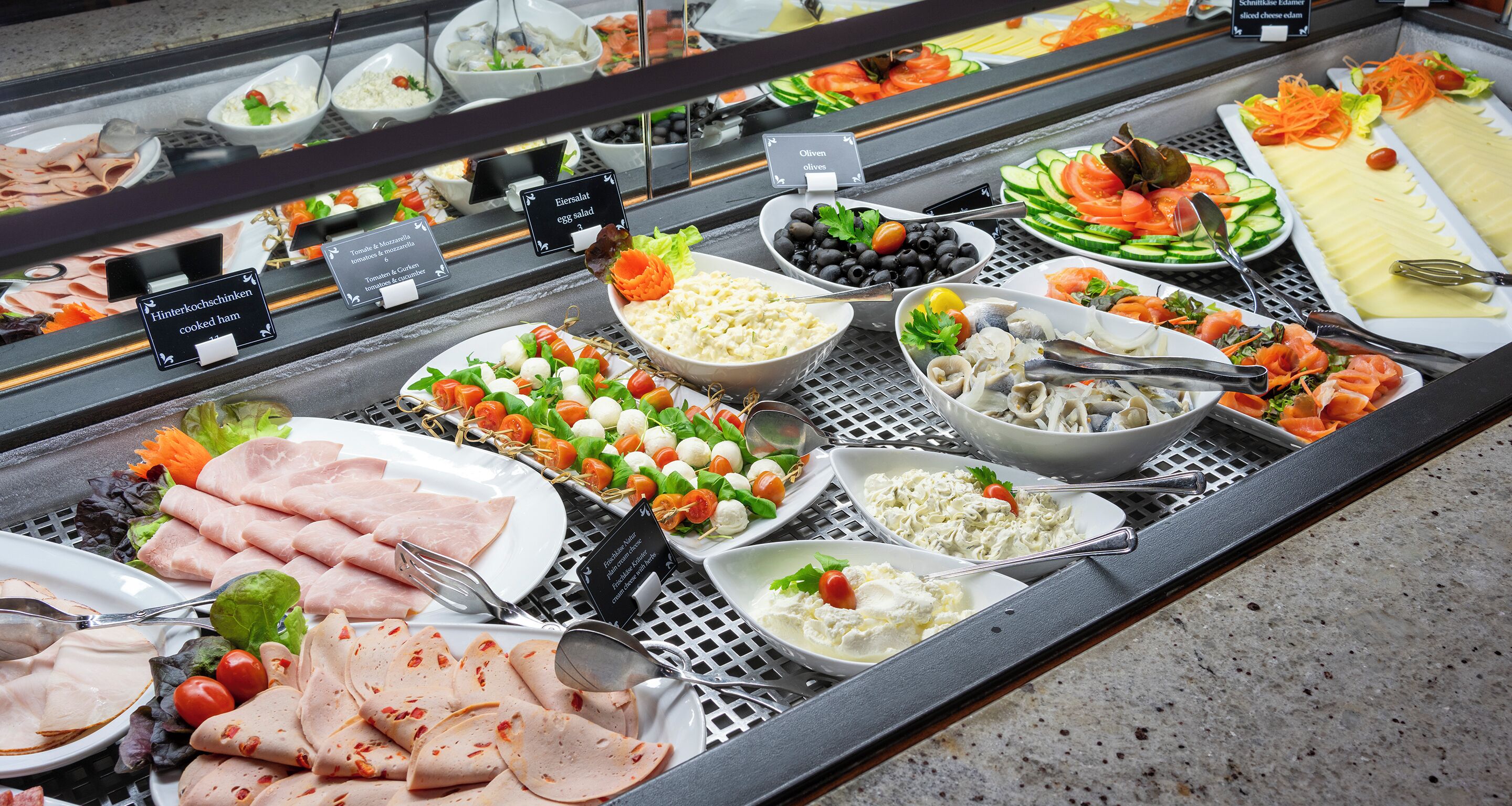 A buffet with various food items including meats, salads, and cheeses.