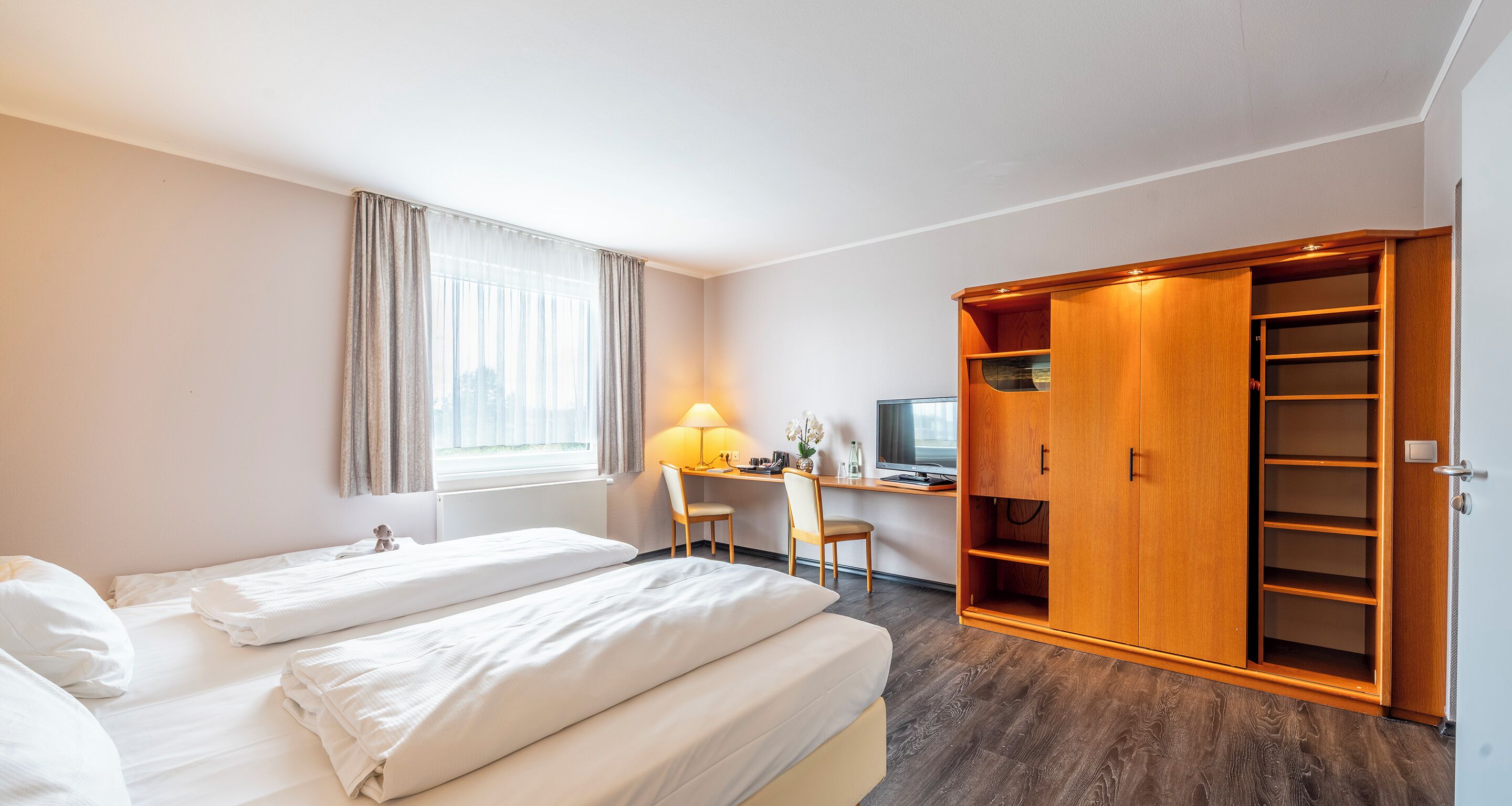 Ein Hotelzimmer mit zwei Betten, einem Schreibtisch mit Computer, einem Fernseher und einem Kleiderschrank.