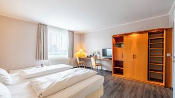 Ein Hotelzimmer mit zwei Betten, einem Schreibtisch mit Computer, einem Fernseher und einem Kleiderschrank.