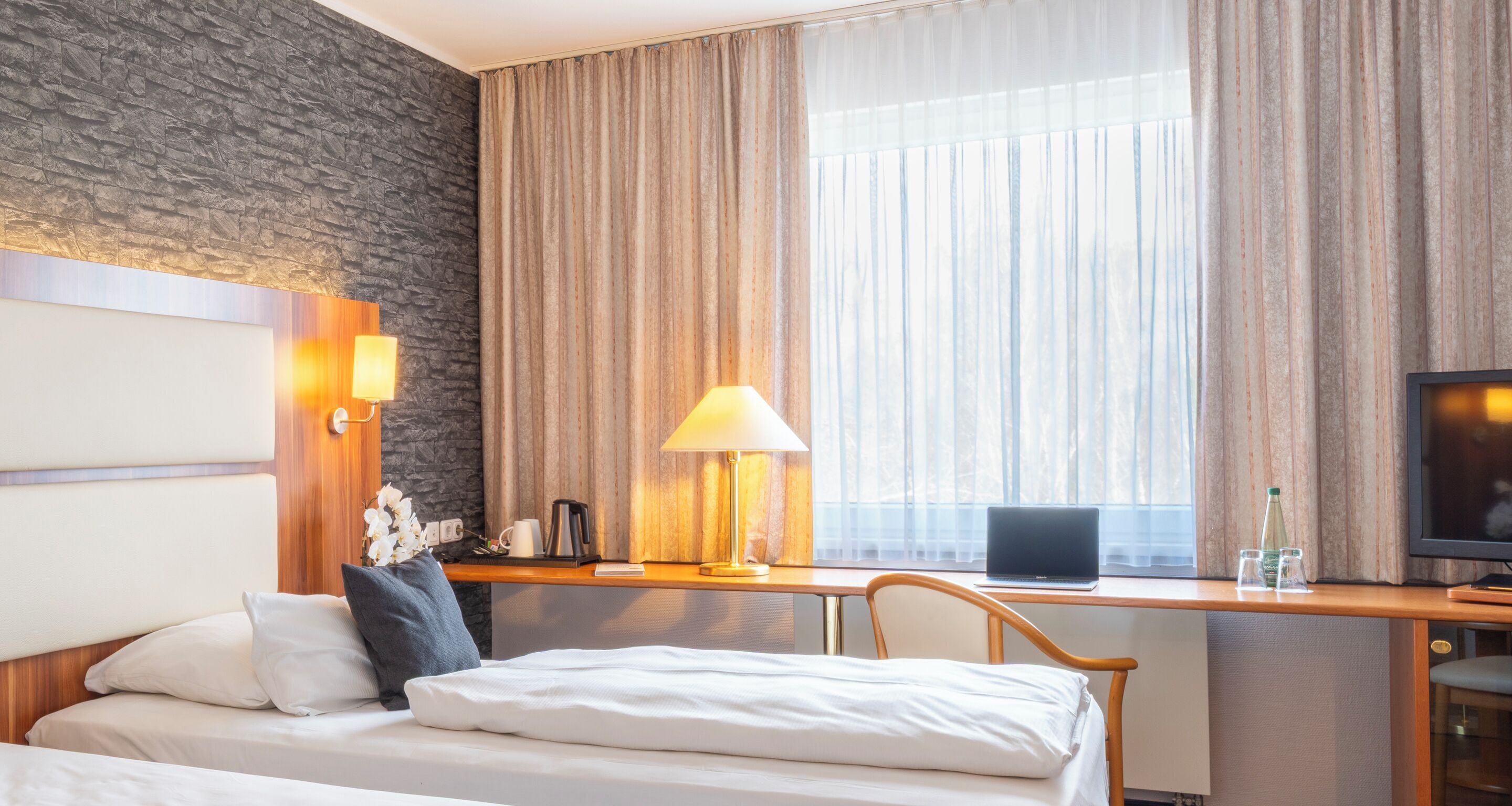 Ein Hotelzimmer mit Bett, Schreibtisch, Laptop, Lampe und Fernseher.