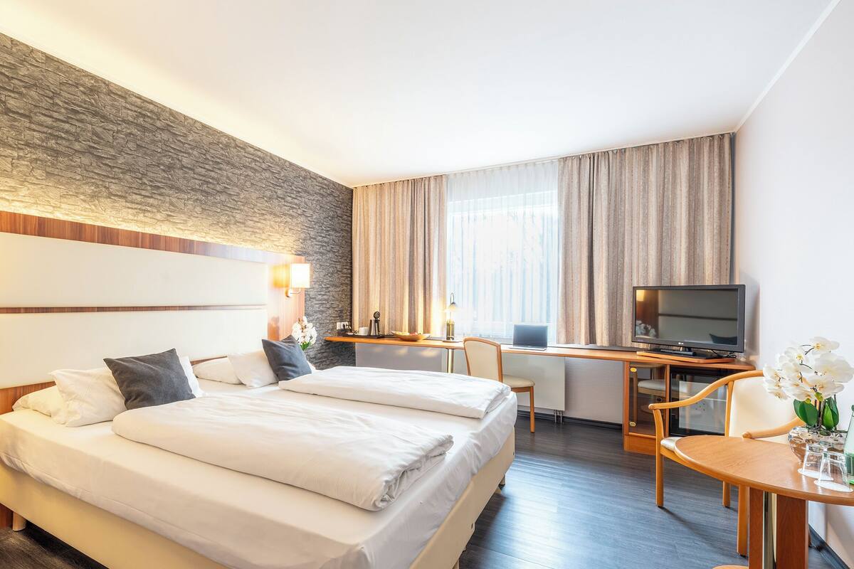 Una habitación de hotel con una cama grande, un escritorio con televisor y una pared de piedra.