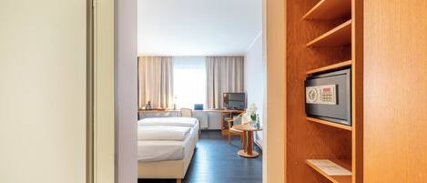 A hotel room with a bed, a desk, a TV, and a wooden shelf.