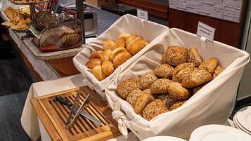 Un buffet proposant une variété de pains et de viennoiseries, notamment des croissants et des petits pains aux céréales.