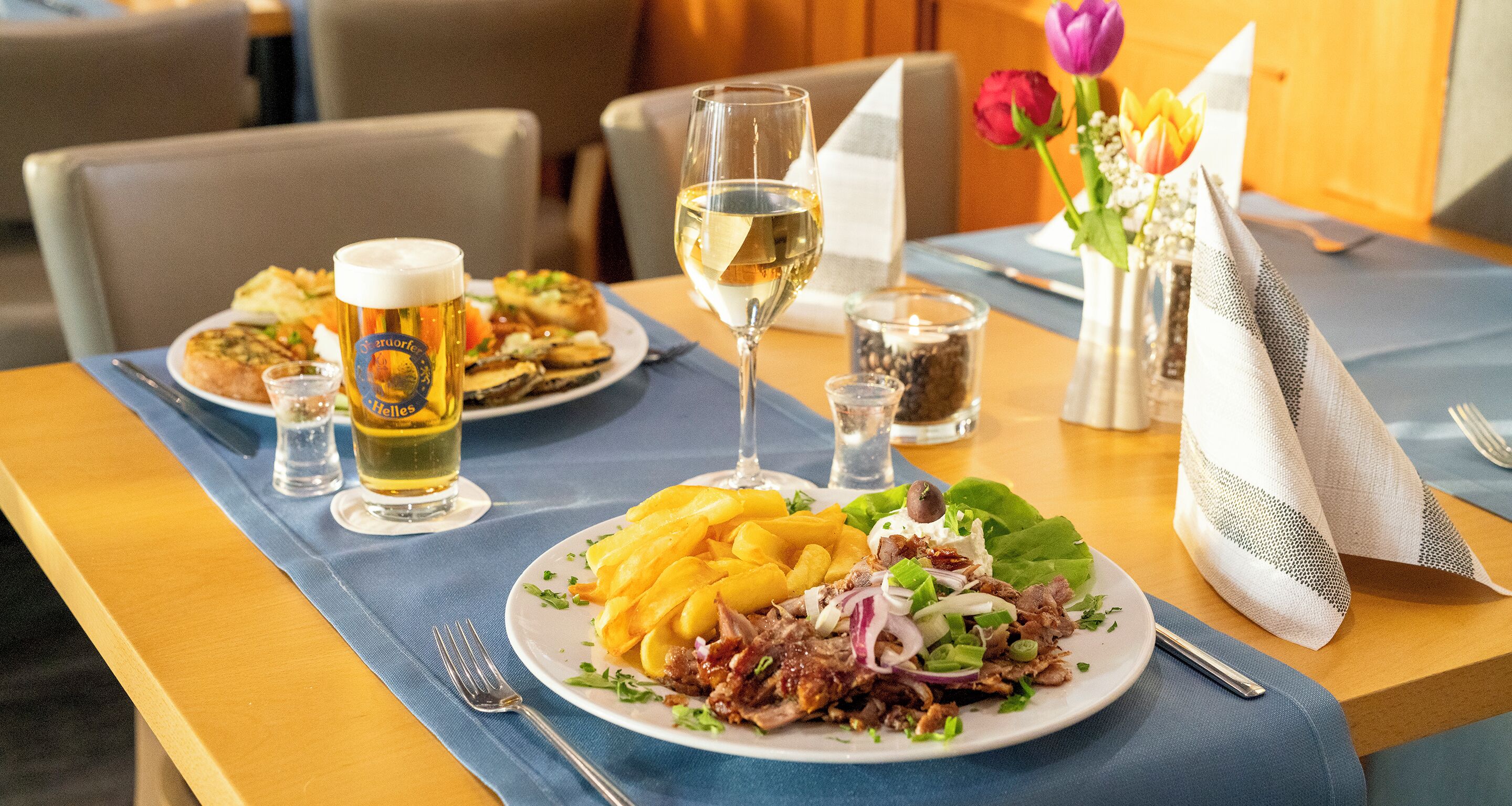 A dining table with plates of food, a glass of white wine, and a beer glass.