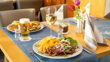 Ein Esstisch mit Tellern voller Essen, einem Glas Weißwein und einem Bierglas.