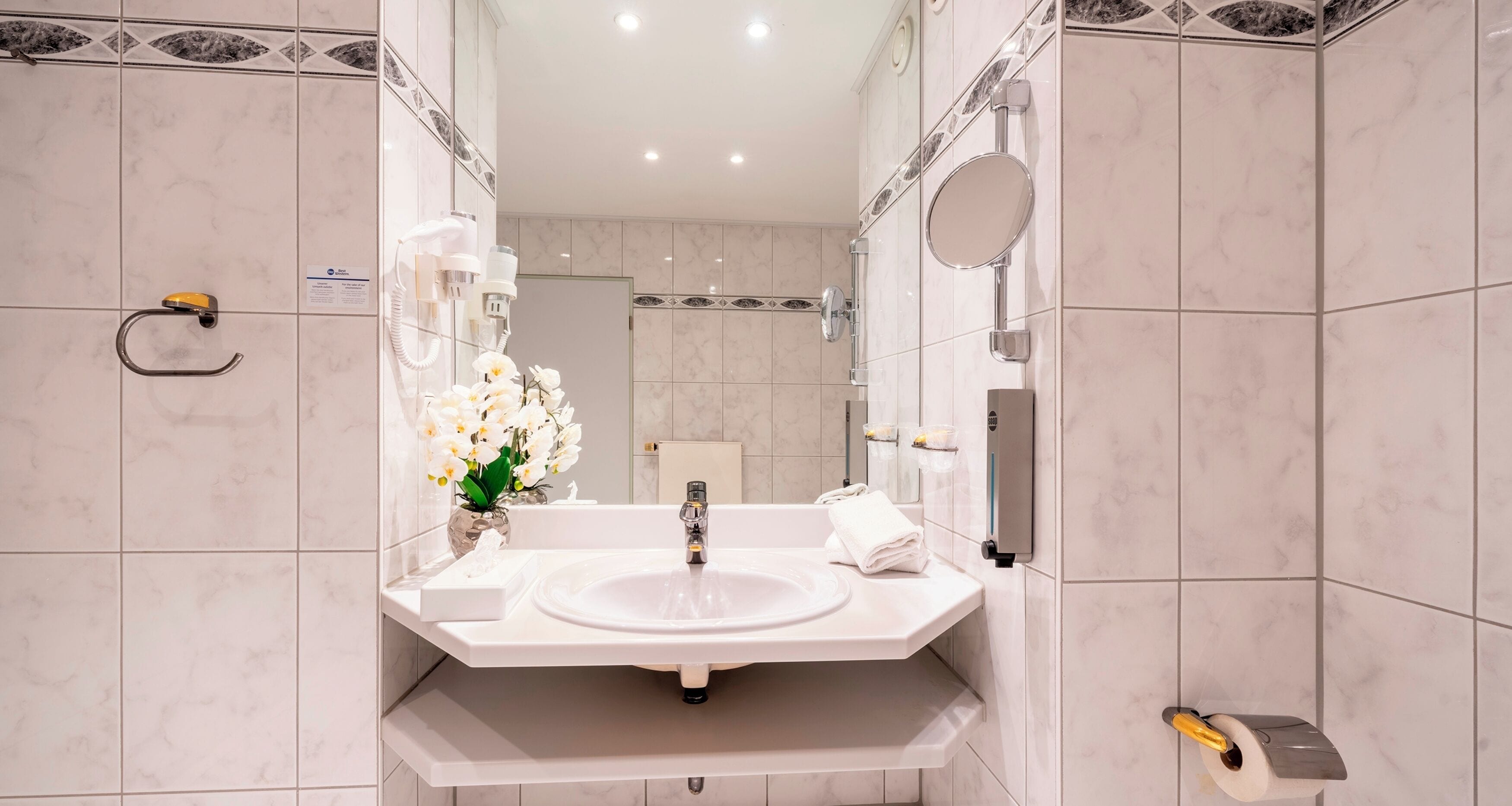 A modern bathroom with a white sink, a mirror, and a vase of white flowers.