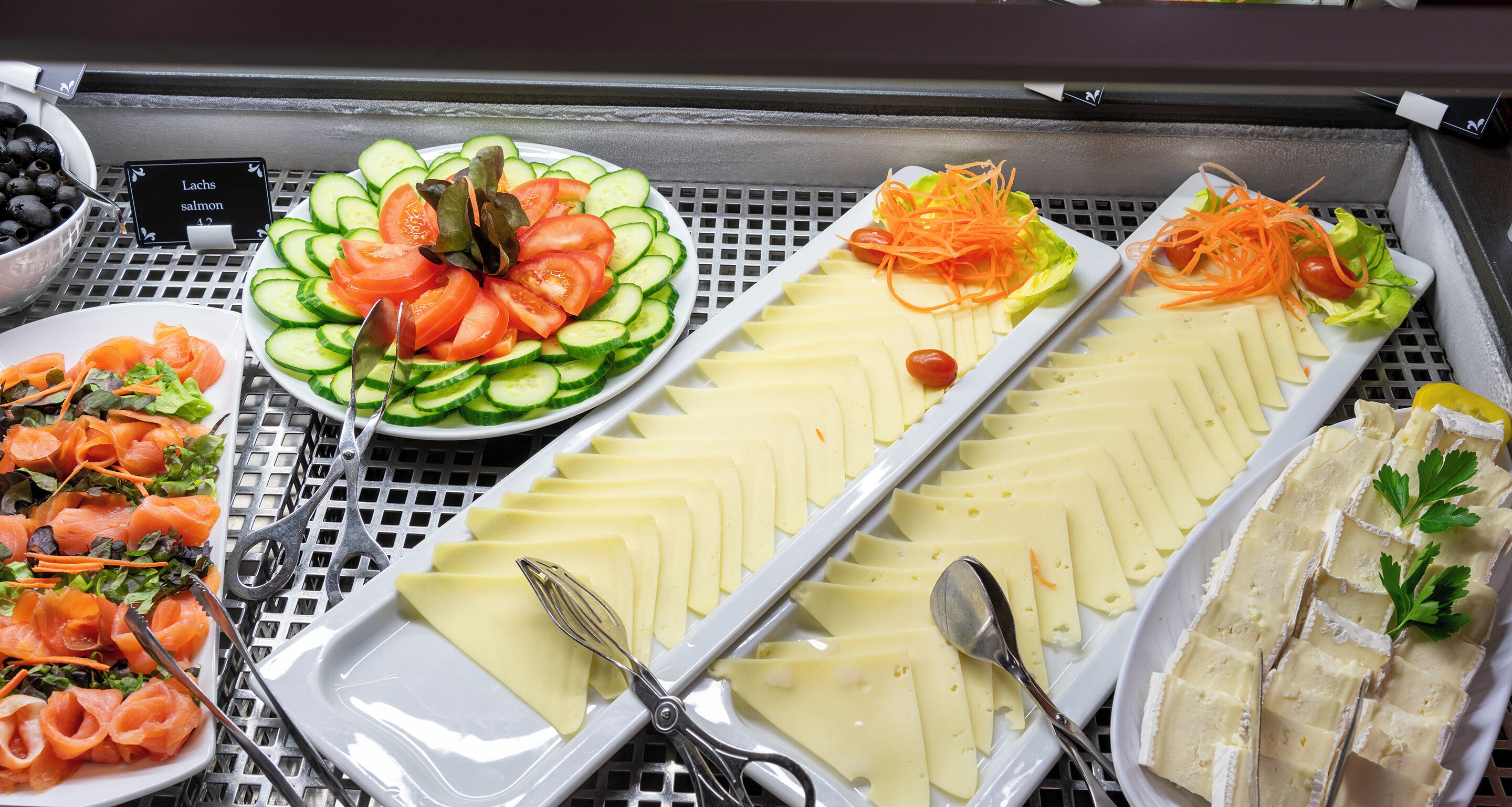 Un bufé con diferentes opciones de comida, incluyendo pepinos en rodajas, tomates y queso.