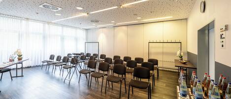 Une salle de conférence avec des rangées de chaises, une table avec des bouteilles d’eau et une horloge au mur.