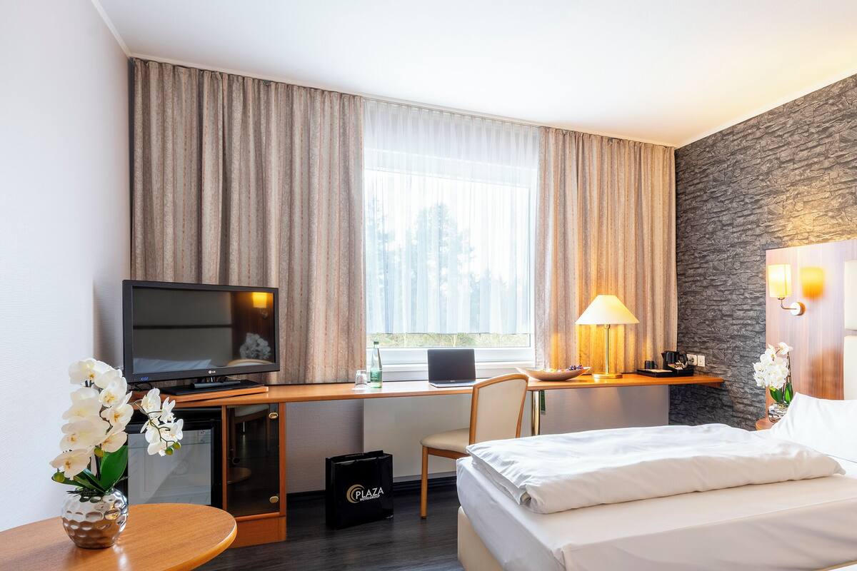 Habitación de hotel con cama, escritorio con una computadora portátil, televisor y pared decorativa de piedra.