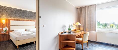 Habitación de hotel con una cama, un escritorio con una silla, una lámpara y vistas a zonas verdes.