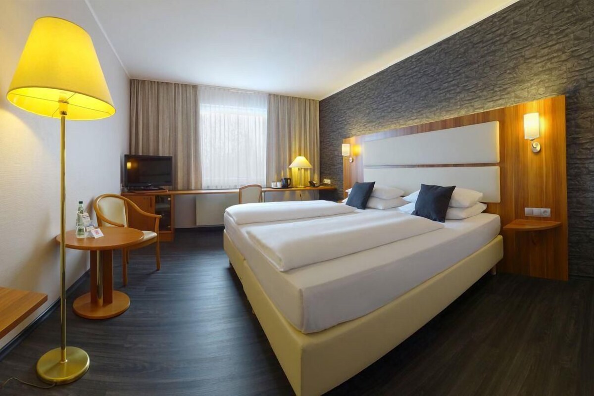 Ein Hotelzimmer mit einem großen Bett, einem Schreibtisch mit Stuhl, einem Fernseher und einer Lampe.