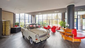 Ein Oldtimer in einer modernen Lobby mit großen Fenstern, roten Sesseln und einem Holzbüro.