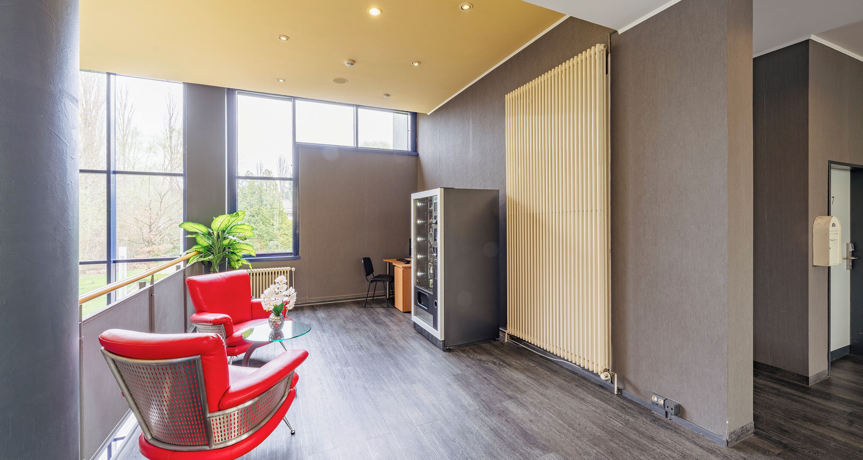 A modern hotel room with a large window, a red chair, a small table, and a radiator.