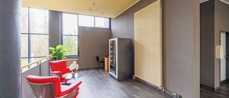 A modern hotel room with a large window, a red chair, a small table, and a radiator.