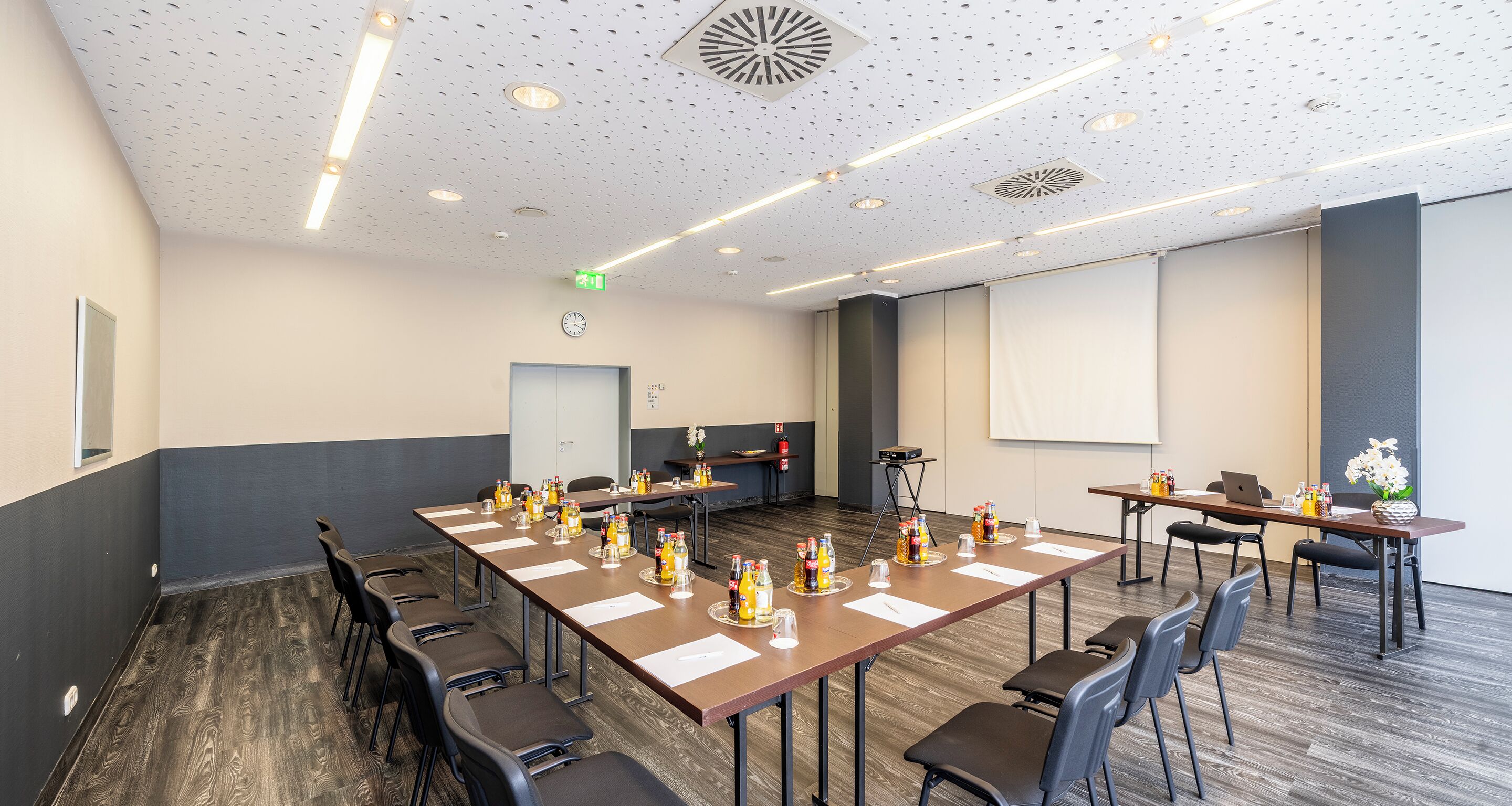 Una sala conferenze con lunghe tavolate, sedie e schermi per presentazioni.