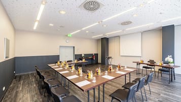 Una sala conferenze con lunghe tavolate, sedie e schermi per presentazioni.