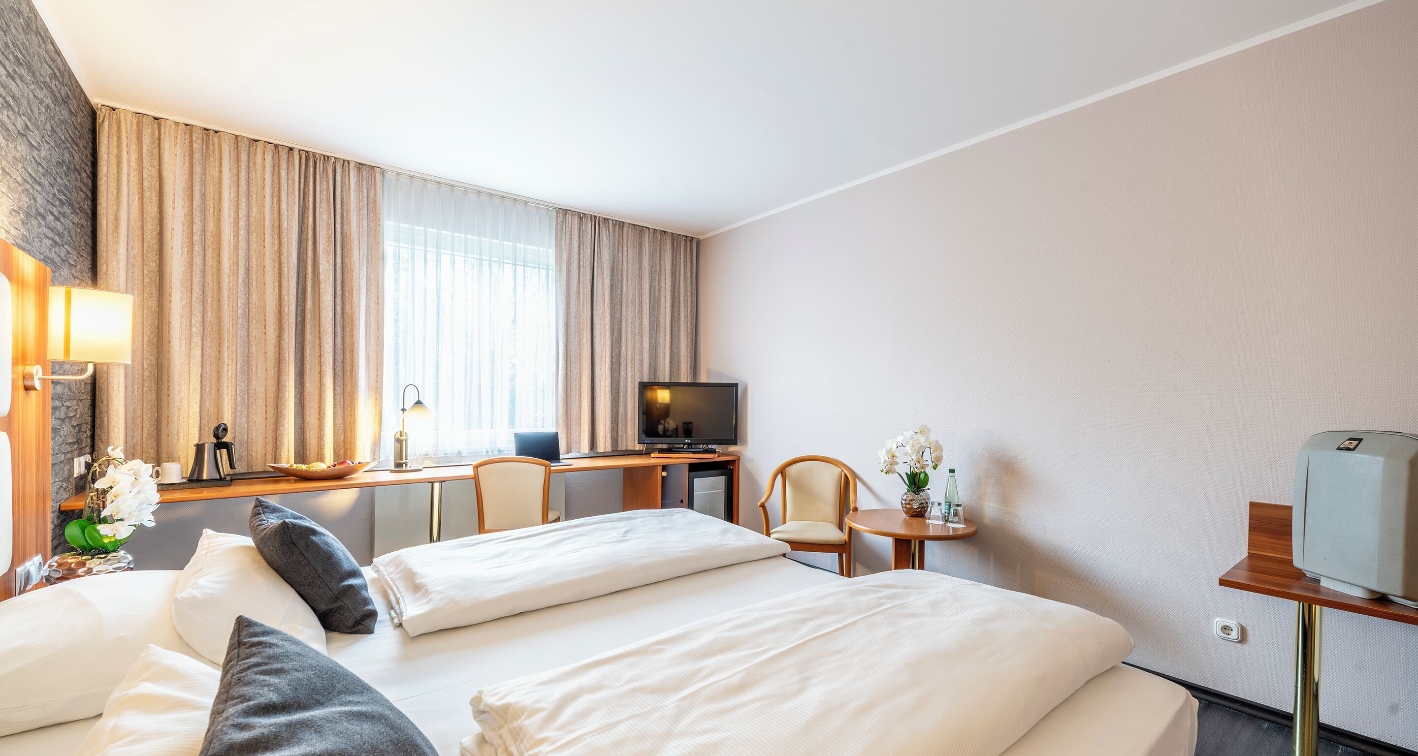 Una habitación de hotel con cama, escritorio, televisor y una mesita con un florero.