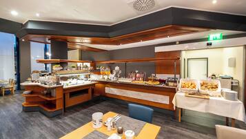 A breakfast buffet area with a variety of food items, a coffee station, and seating arrangements.