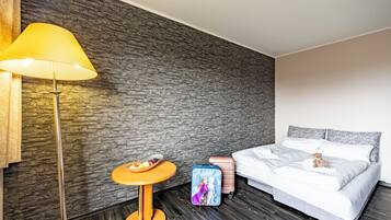 Hotelkamer met een stenen muur, een bed met witte lakens, een klein tafeltje met fruit, een lamp en een koffer.