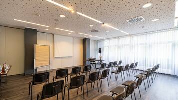 Een vergaderzaal met rijen stoelen, een scherm voor een beamer en een tafel met waterflesjes.