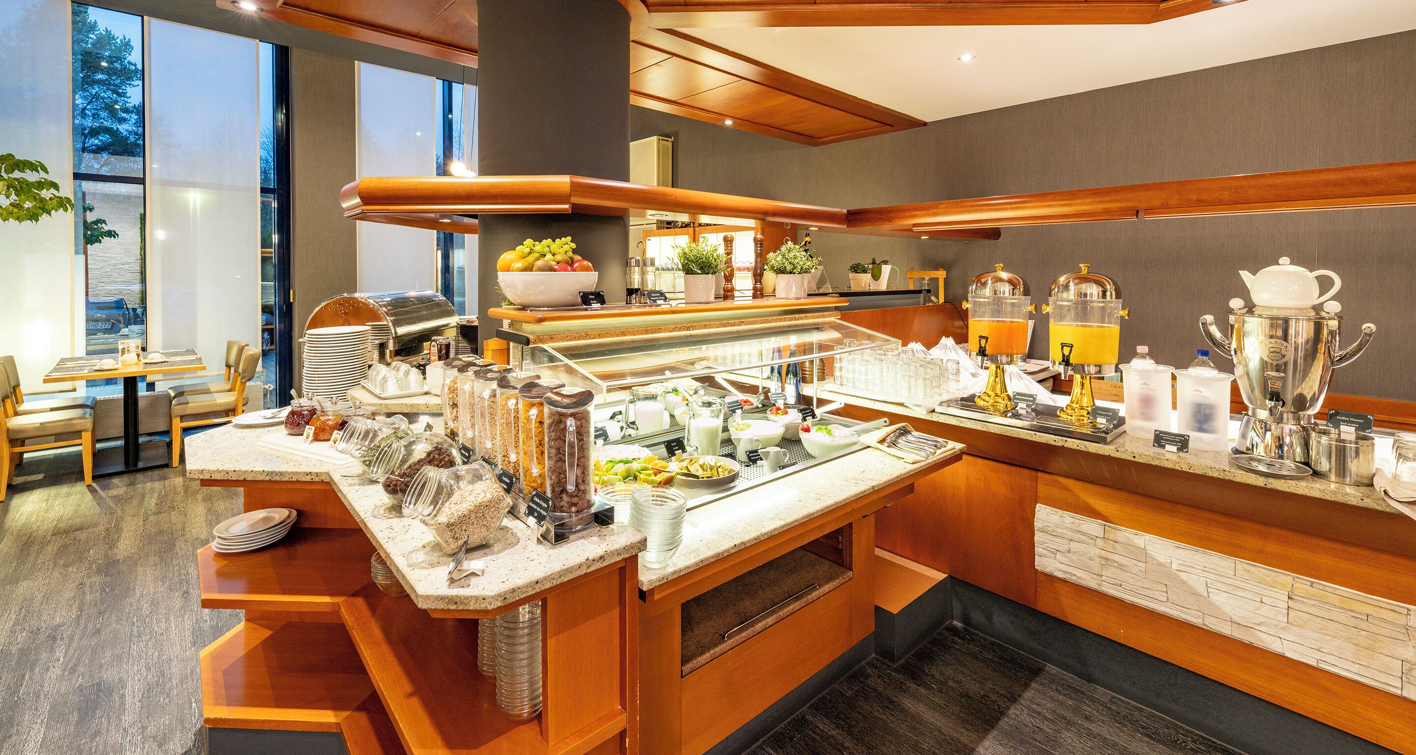 A modern breakfast bar with a variety of food and drink options, including fruits, cereals, and coffee machines.
