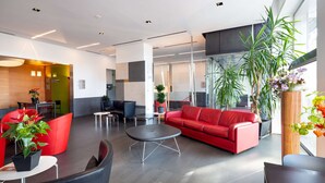 A modern lobby with a red sofa, black chairs, a round table, and potted plants. - Best Western Hotel Major (Milan)