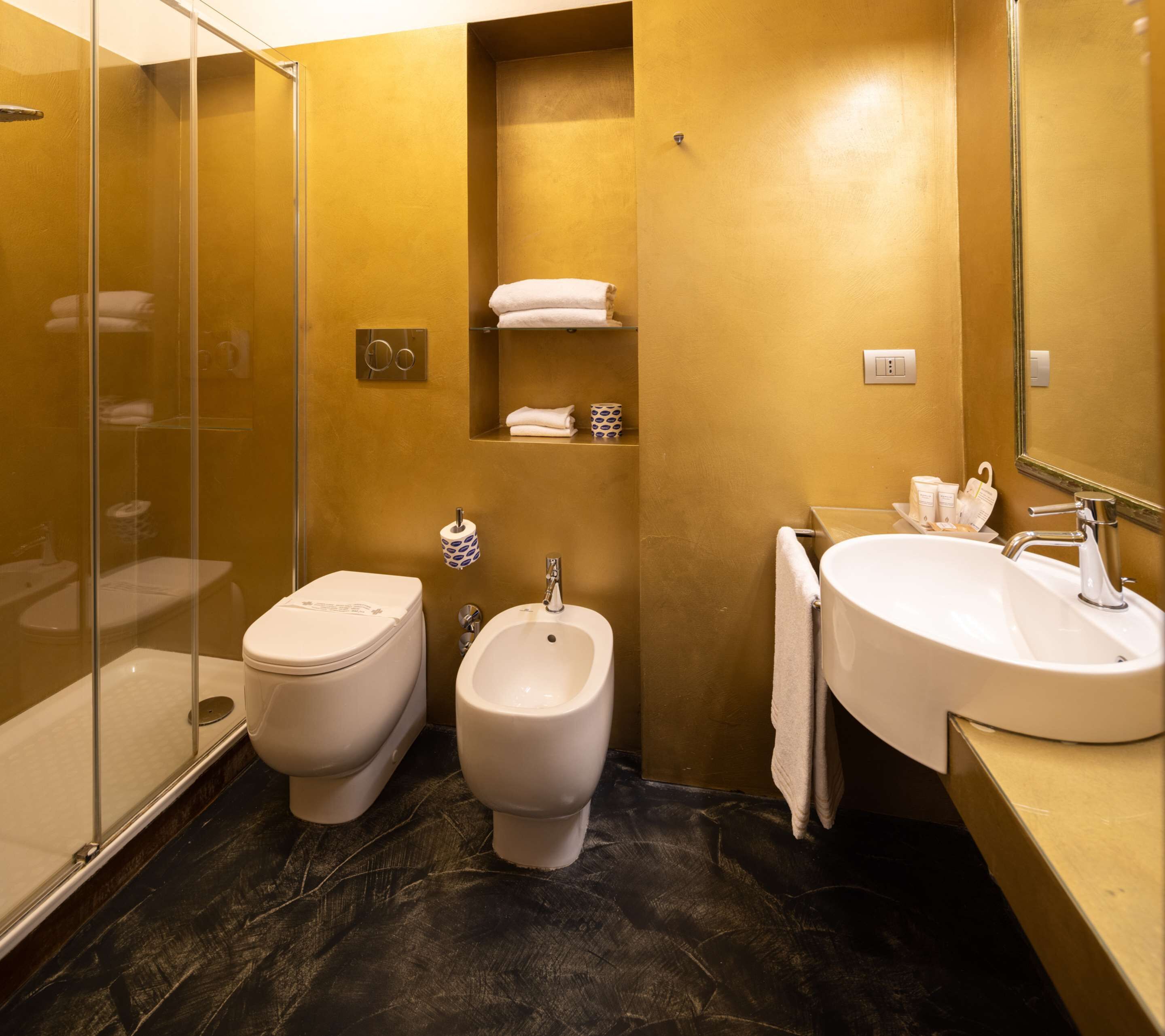 Een badkamer met een douchecabine van glas, een toilet, een bidet en een wastafel met spiegel.
