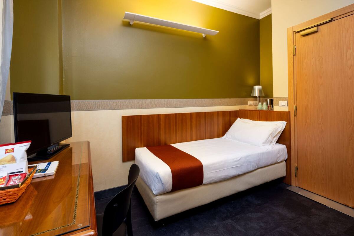 A hotel room with a bed, desk, TV, and a wooden wardrobe.