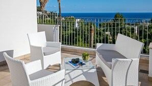 A balcony with white wicker furniture, a glass table, and a view of the sea.