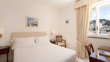 A hotel room with a bed, a chair, a small table, and a window with curtains.