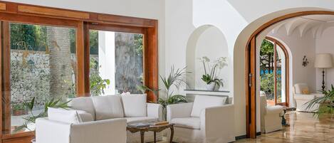 A spacious living area with a large window, a white sofa set, a coffee table, and a polished marble floor.