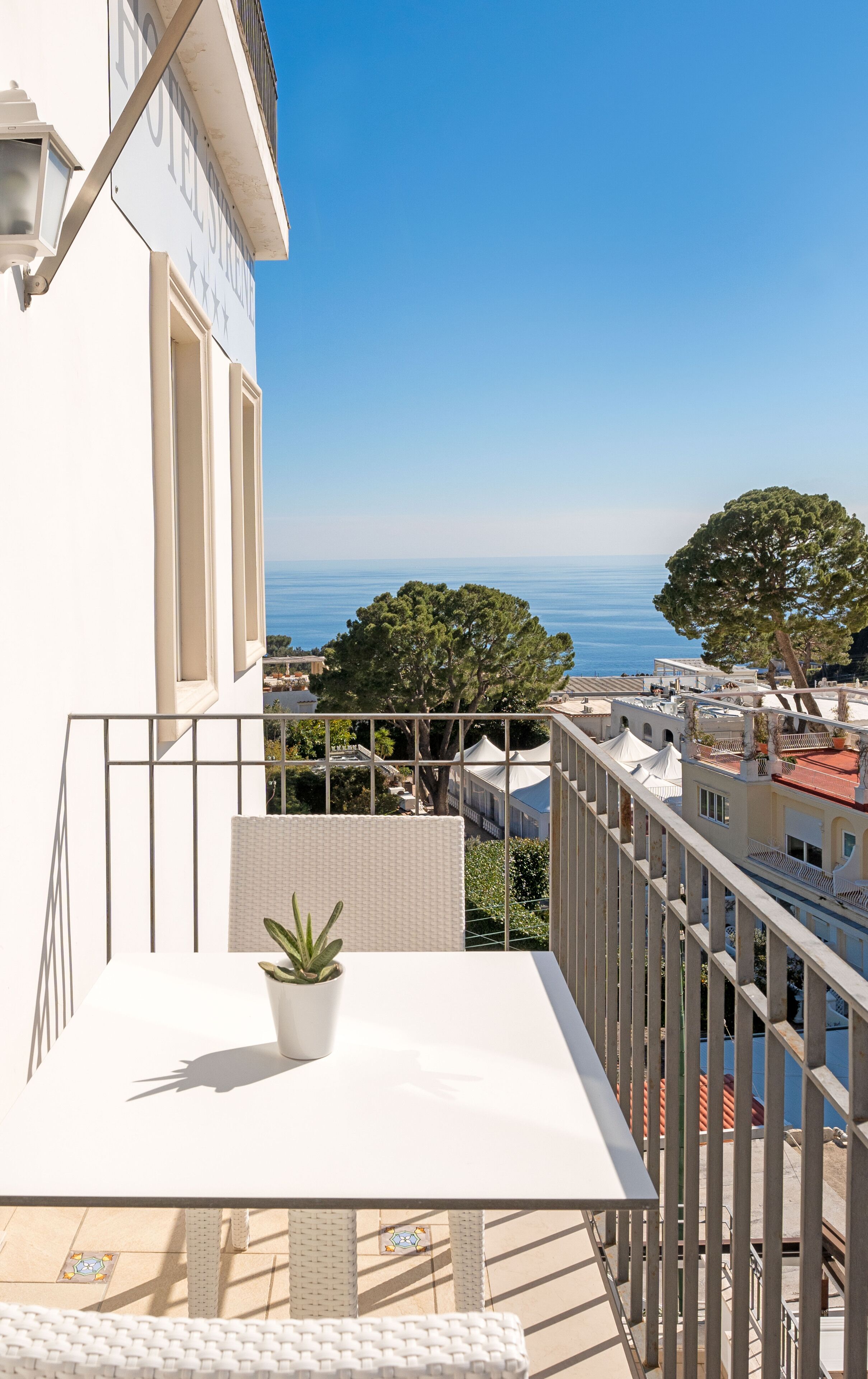 A balcony with a potted plant, overlooking a cityscape and the sea.