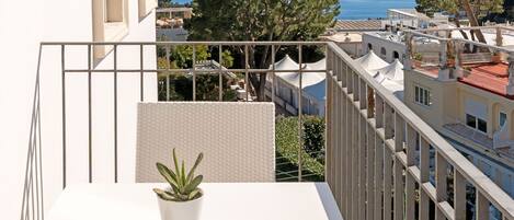 A balcony with a potted plant, overlooking a cityscape and the sea.