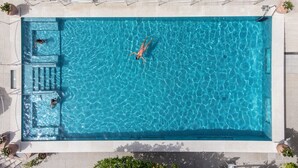 A rectangular swimming pool with clear blue water, surrounded by white lounge chairs and a tiled deck.