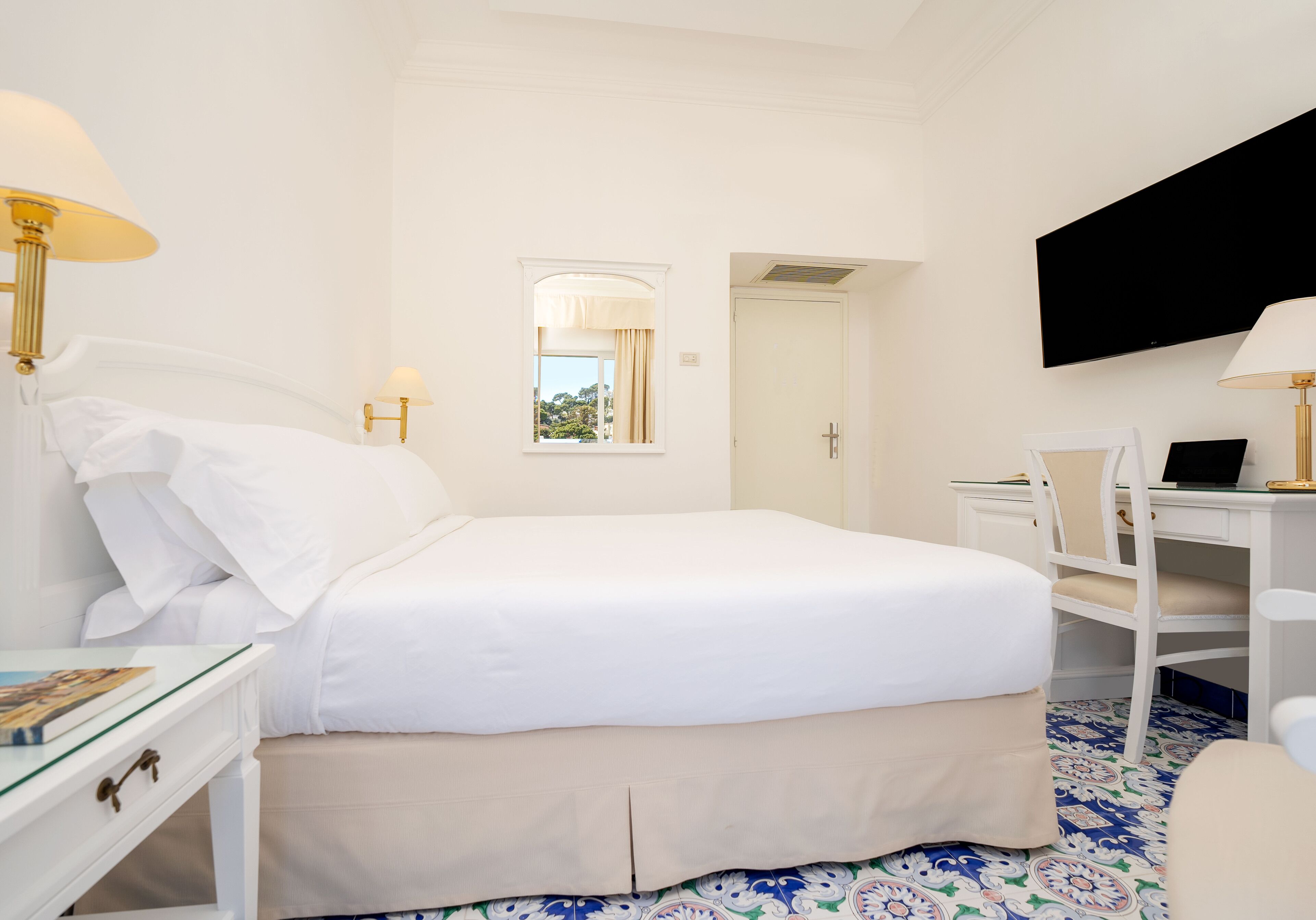 A hotel room with a bed, a desk, a chair, a TV, and a window with curtains.
