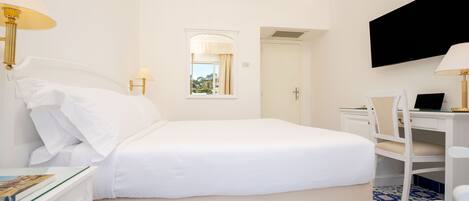 A hotel room with a bed, a desk, a chair, a TV, and a window with curtains.