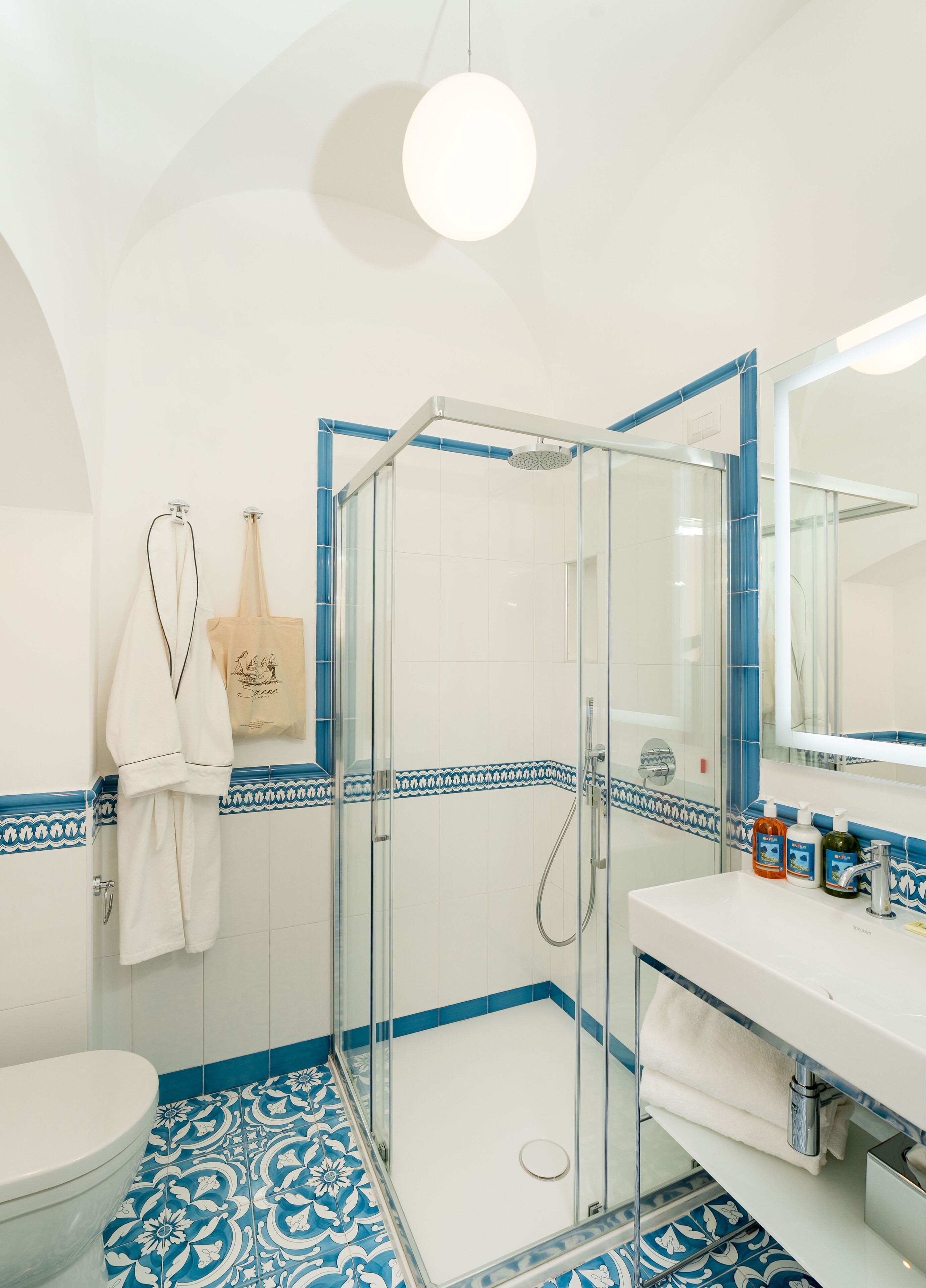 Un bagno con doccia vetrata, lavandino bianco con articoli da toilette e pavimento decorato.