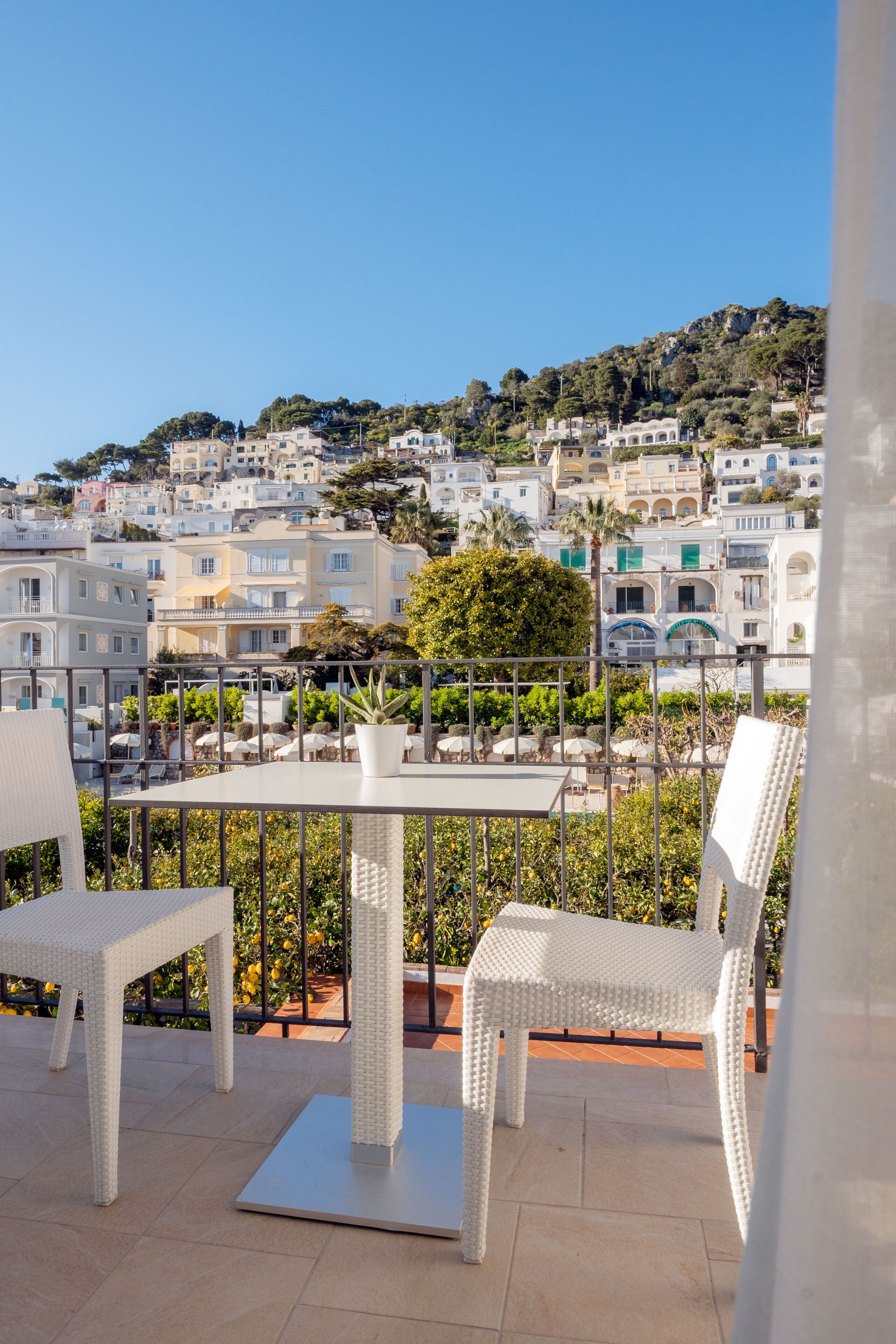 A terrace with wicker furniture, a table, and a view of a hillside town.