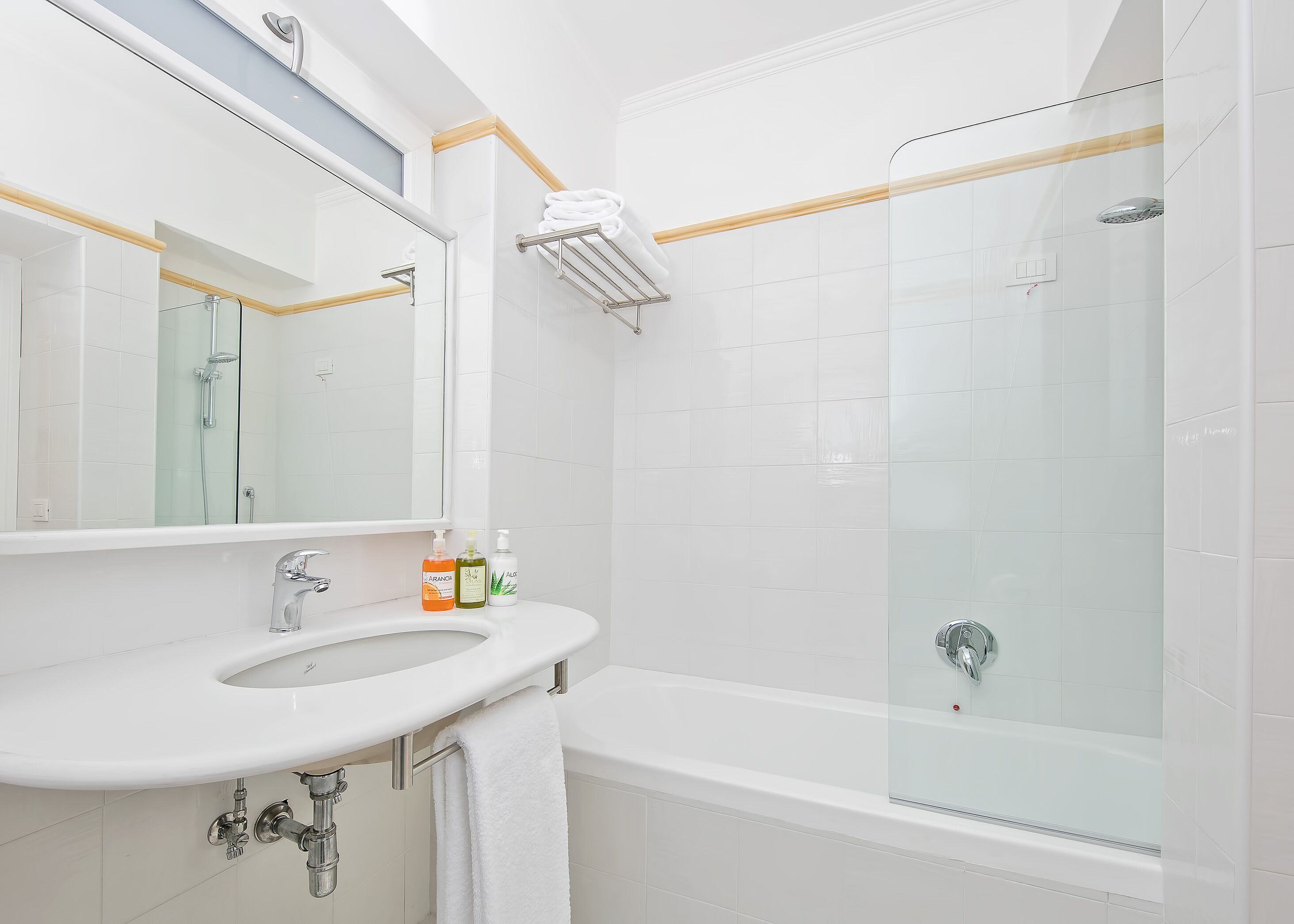 A modern bathroom with a white sink, mirror, and glass-enclosed shower.