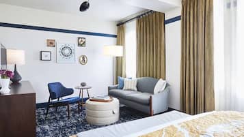 A hotel room with a bed, a sofa, a chair, a small table, and a lamp.