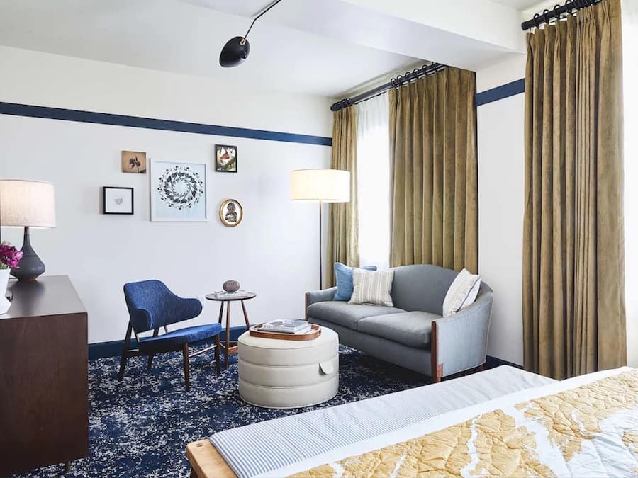 A hotel room with a bed, a sofa, a chair, a small table, and a lamp.