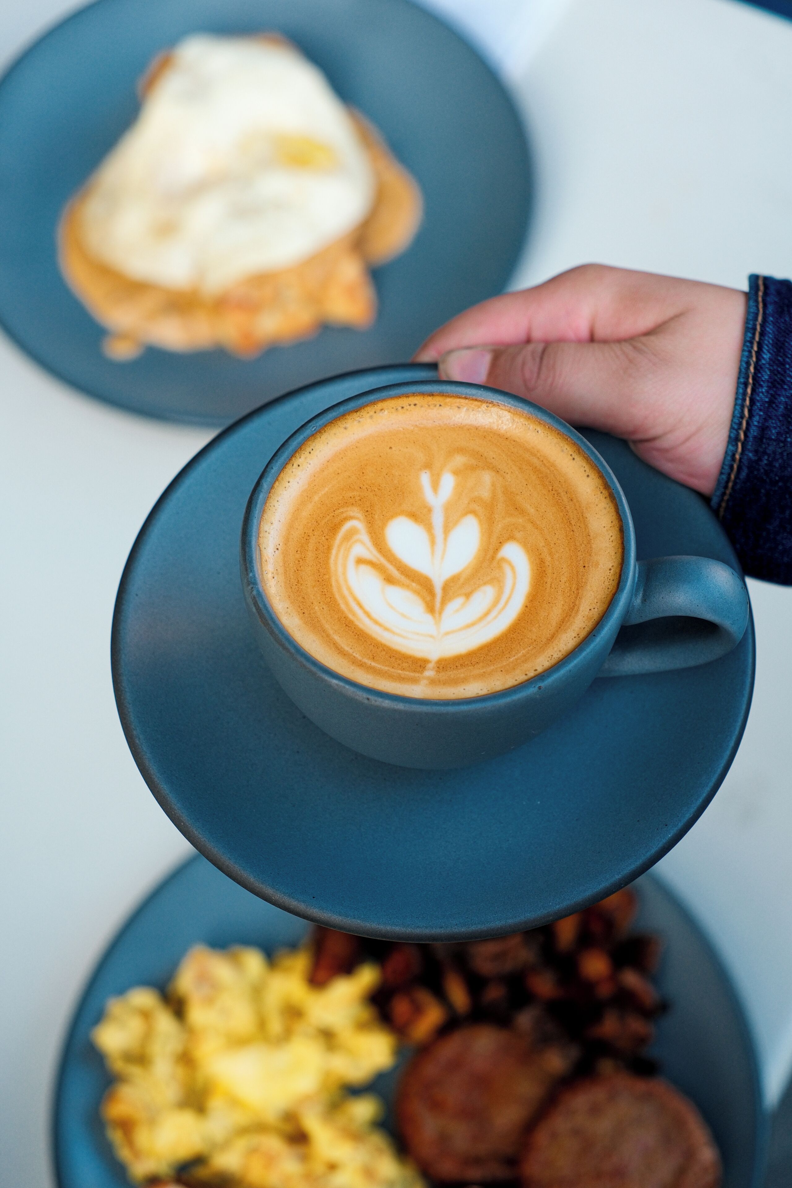 A hand holding a cup of coffee with latte art on a saucer.
