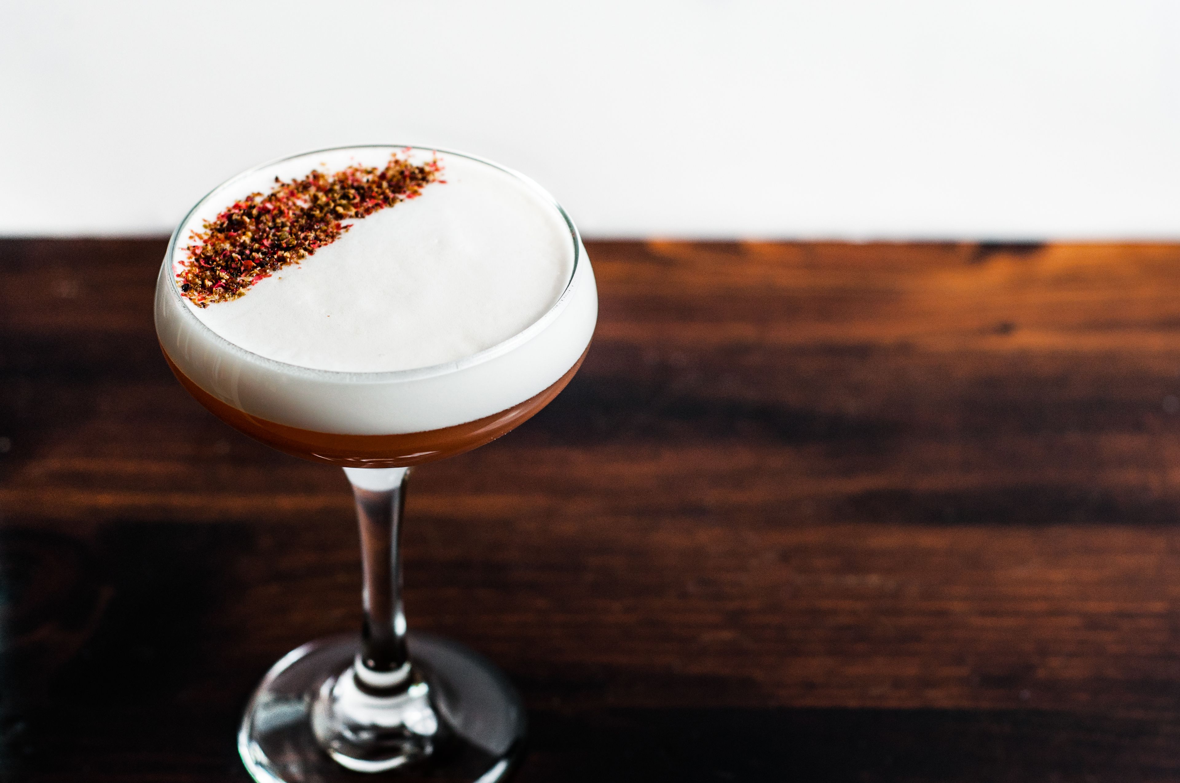 A cocktail in a stemmed glass with a salted rim, placed on a wooden surface.