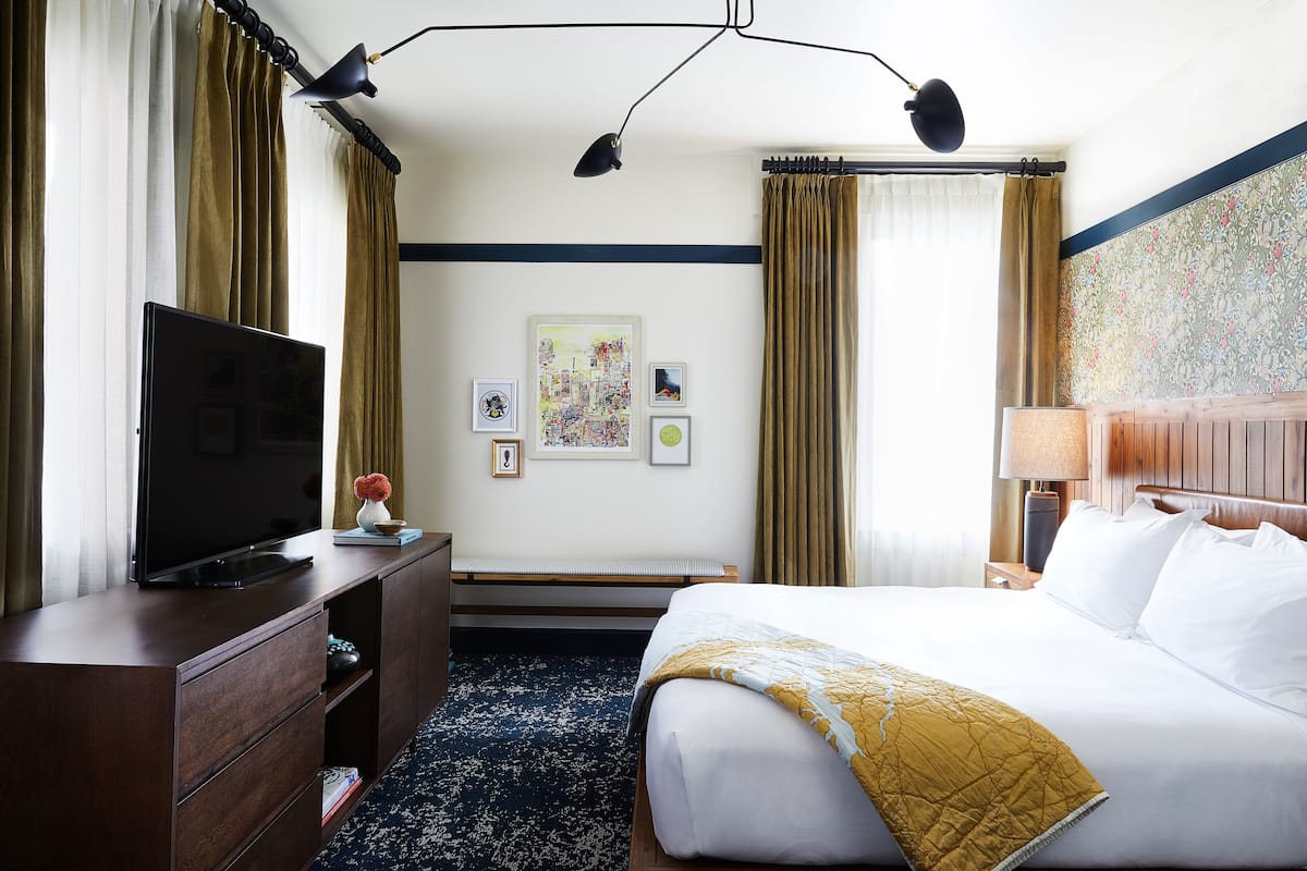 A hotel room with a bed, a TV on a wooden dresser, a desk, and a nightstand.