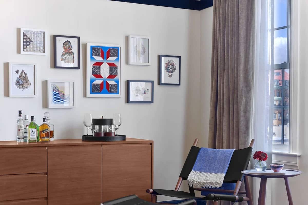A room with a wooden cabinet, a chair with a blue throw, and a small table with a vase and a bowl.
